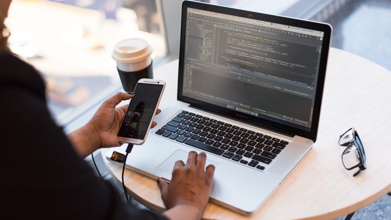 person-looking-at-phone-and-at-macbook-pro-1181244